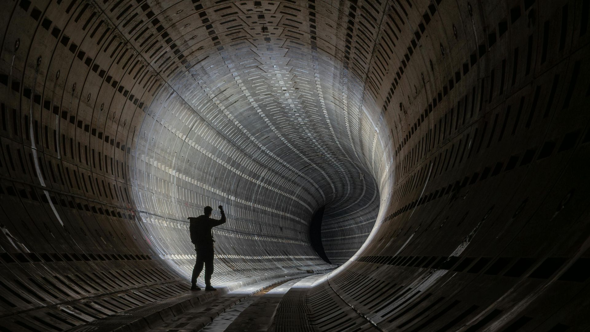 A single silhouette inside a vast tunnel, looking down its length — visualising the narrow viewpoint of a single AI.